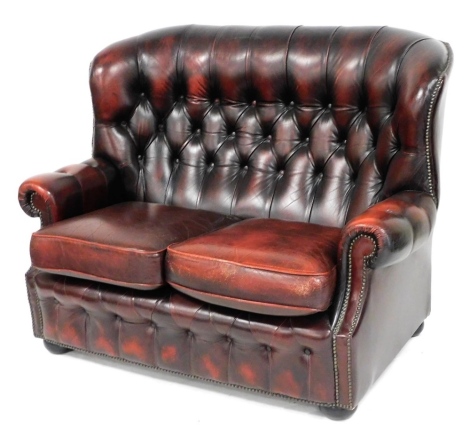 A two seater red ox blood leather sofa, with button back and front, loose cushion seats, raised on bun feet, 129cm wide.