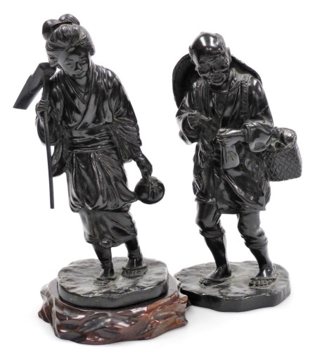 A pair of Japanese Meiji period bronze Tokyo School figures, of a lady holding a hoe and teapot, and man with pipe and tobacco pouch, four character signature of Genryusai Seiya to each base, each figure 26cm high, one hardwood base.