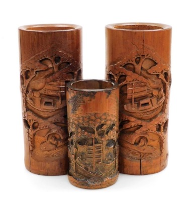 A pair of 20thC Chinese bamboo brush pots, carved in relief with trees, figures and boats, 28cm high, and a further smaller example, 18cm high. (3)