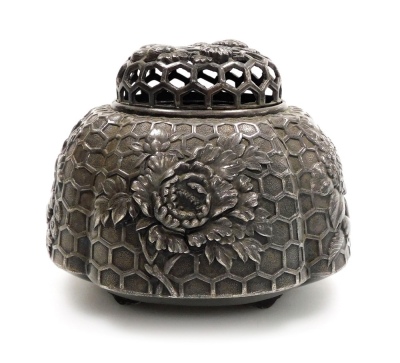 An early 20thC Japanese white metal koro and cover, with high relief floral decoration on a relief honeycomb background, all on four feet, 8cm high.