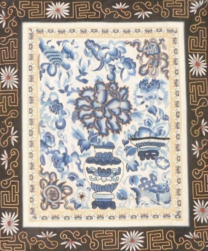 A Chinese silk embroidered panel, in blue and white depicting vase and bowl on stand with flowers, within an elaborate brocade border, 42cm x 35cm.