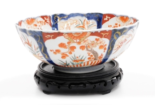 A 19thC Japanese Imari bowl, of fluted form, 25cm diameter, on hardwood stand.