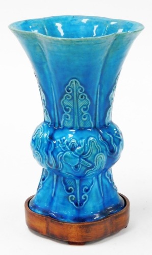 A 19thC Chinese turquoise ground porcelain Gu vase, decorated in relief with precious objects and lappets, 21cm high, with hardwood stand.