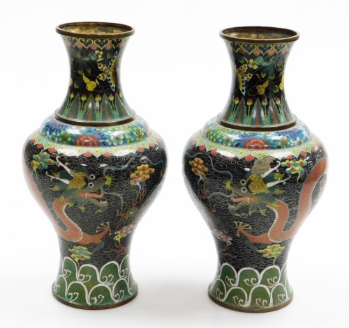 A pair of late 19thC Chinese cloisonne enamel vases, with brass rims, decorated with Imperial dragons in the clouds chasing a flaming pearl, on a black ground, within floral and acanthus leaf borders, 32.5cm high.