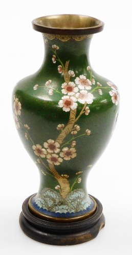 A Chinese cloisonne enamel vase, with brass rims, of baluster form, decorated with prunus blossom on a green ground, 22.5cm high, on a hardwood stand. (AF)