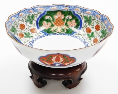 A Japanese Kenjo style Imari porcelain bowl, painted with reserves of flowers, and scrolling leaves, blue printed flower mark, 18.5cm diameter, on a hardwood stand.