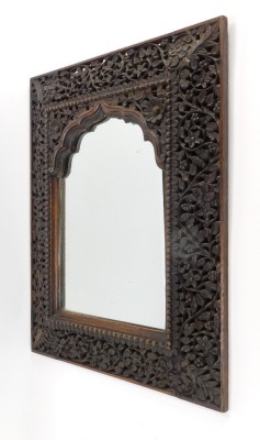 A Burmese carved wooden wall mirror, with pierced and fret carved border, with a rectangular arched top mirror plate, 51cm high, 34cm wide.