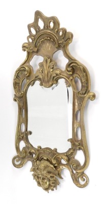 A late 19thC brass rococo wall mirror, the shell cast top with Medusa figure, 58cm high, 32cm wide.