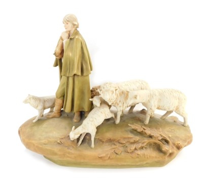 A Royal Dux figure group of sheep and a shepherdess with water vessel, the shepherdess modelled stood on a grassy bank, wearing a cloak, trousers, and boots, a hat clasped between his hands, a sheep dog stood to his right, and a ram, ewe and two lambs sto