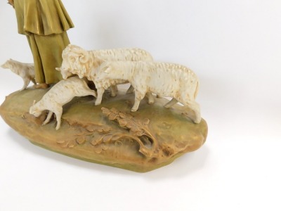 A Royal Dux figure group of sheep and a shepherdess with water vessel, the shepherdess modelled stood on a grassy bank, wearing a cloak, trousers, and boots, a hat clasped between his hands, a sheep dog stood to his right, and a ram, ewe and two lambs sto - 2