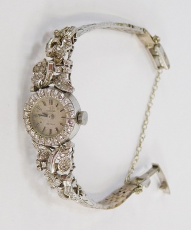 An Omega De Ville lady's wristwatch, with small silvered dial and elaborate diamond set border and leaf design shoulders, in white metal stamped 18k to clasp, the dial 1cm wide, 22g all in.