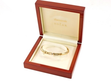 A Diamond by Solar 9ct gold bangle, the central diamond in a rub over setting, with two strand panel clip, 6.7g all in, 6cm diameter, boxed with certificate.