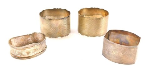 Four silver napkin rings, comprising a pair of George V engine turned decorated napkin rings, one with crest 31-1-56, another bearing the initials RMM, a mishapen Victorian napkin ring, with initials DCJ, and a rectangular set example with vacant shield, 