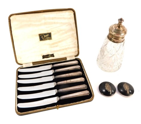 A cased set of F Butcher silver handled butter knives, boxed, a pair of ebonised and silver topped dressing table jar lids and a cut glass and silver topped shaker, Chester 1908. (4)