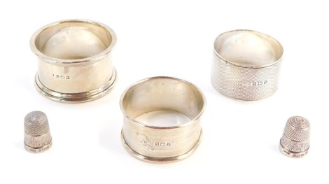 Three silver napkins rings and two silver thimbles, the napkin ring George VIII and later, one with engine turned hatch detail land vacant crest, another of ribbed and overlaid design, and a plain example, 1¾oz. (5)