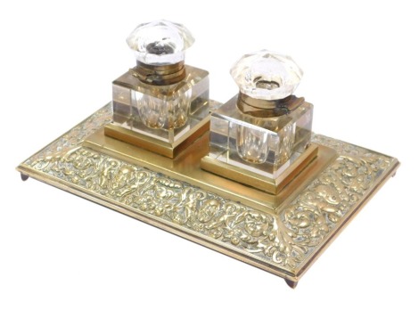 A late 20thC brass desk stand, the central rectangular panel, with two cut glass inkwells, with scroll and foliate design order, on four cap feet, 12cm high, 22cm wide, 14cm deep.