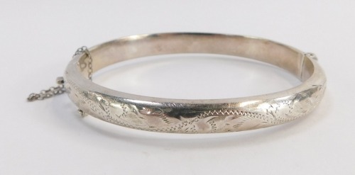 A Victorian silver hinged bangle, the half hinged designed with engraved scroll decoration and safety chain, 6cm diameter.