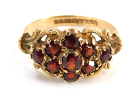 A 9ct gold dress ring, the cluster section set with garnets with scroll design shoulders, size L½, 3.2g all in.