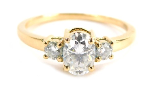 A three stone dress ring, set with three moissanites, comprising a large oval moissanite in four claw setting flanked by two round brilliant cut moissanites, in a raised basket, yellow metal stamped 18k, size P½, 3g all in, boxed.