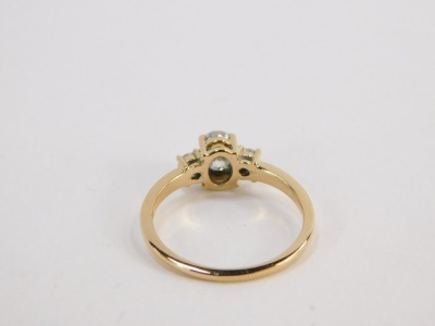 A three stone dress ring, set with three moissanites, comprising a large oval moissanite in four claw setting flanked by two round brilliant cut moissanites, in a raised basket, yellow metal stamped 18k, size P½, 3g all in, boxed. - 2