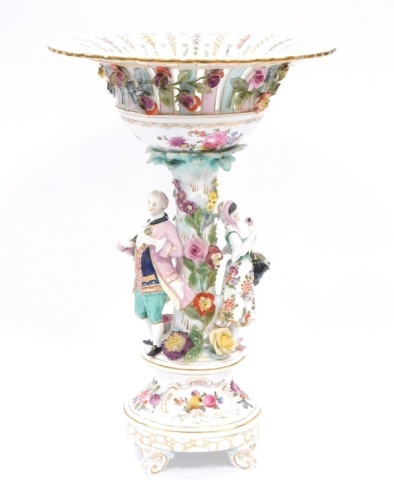 A Dresden porcelain centrepiece, the elaborately decorated fluted and pierced top in pink and turquoise with gilt detail, applied flowers and figure of lady and gentleman to stem, on scroll feet, 42cm high.