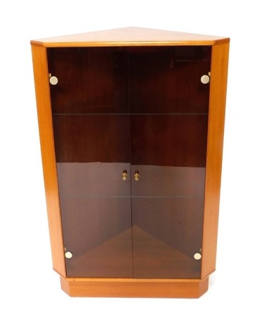 A Turnbridge of London teak corner cabinet, with two smoky glass panels and two shelves, bearing Turnbridge of London Limited labels to reverse, 123cm high, 77cm wide, 56cm deep. WARNING! This lot contains untested or unsafe electrical items. It is supp