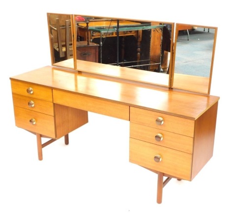 A 1970's teak dressing table, with triple mirror above three drawers to each pedestal flanking a central long drawer, on tapered legs, 122cm high, 145cm wide, 42cm deep.