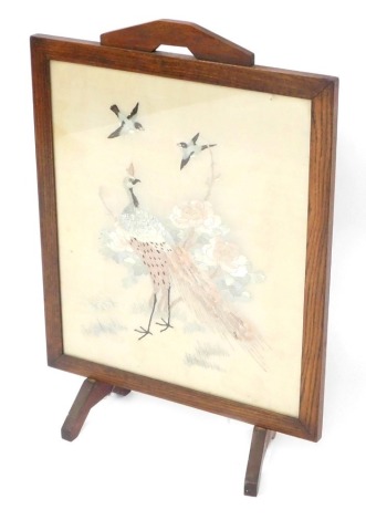 An early 20thC silk lined fire screen, the silk interior with embroidered pattern of stork, bird, and flowers, in an oak frame with swing legs, 73cm high, 51cm wide.