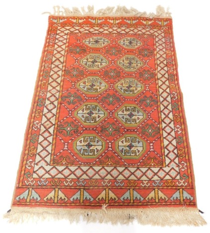 A Persian rug, on a light red ground with ten medallion central section, outer cream border, with tassel ends, 180cm x 100cm.