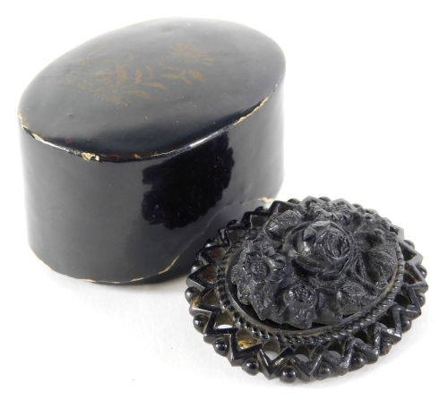 A Victorian carved jet oval brooch, the outer border with triangle cut detail, with rose and daisy applied centre, on a steel pin back, in a papier mache box, the brooch 4cm wide, the box decorated with flower and vine detail, 4.5cm high.