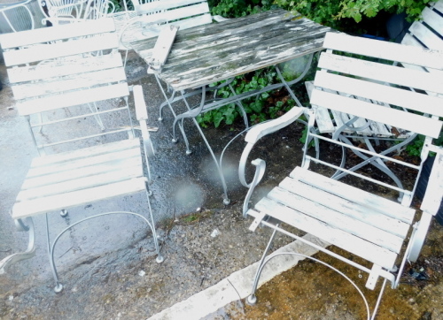 A slatted and silver painted wrought iron garden table and four folding chairs.