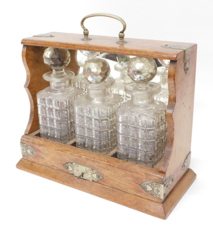 An Edwardian oak cased tantalus, with brass mounts and handle, with thee cut glass bottles, 37cm high, 33cm wide, 23cm deep.