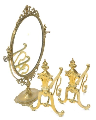 A pair of early 20thC brass fire dogs in Art Nouveau style, 33cm high, and a ornate brass dressing mirror with oval plate, 57cm high.