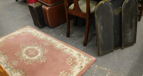 A brass triple fire guard, a fire cover and a pink Chinese rug.