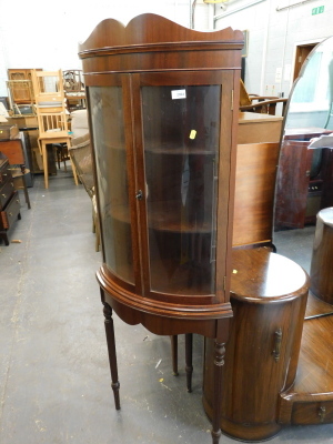 A mahogany bow fronted standing corner cabinet with two glazed doors on turned tapering legs.