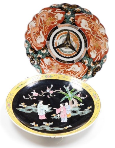 A Japanese Imari charger, decorated with dragons, etc., in typical colours (AF), 40cm diameter, and another Oriental charger, decorated with figures on a black ground within a yellow floral border, 40cm diameter.