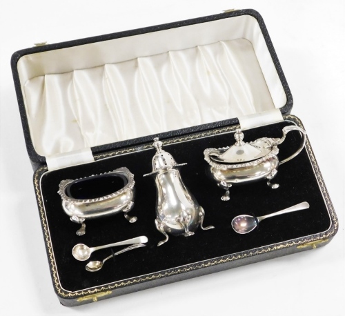 An Elizabeth II silver cruet set, comprising pepper pot, open salt blue glass liner, and mustard pot with blue glass liner, each piece decorated with a scroll and shell cast border, with three associated spoons, Birmingham 1957, weighable silver 4½oz, in