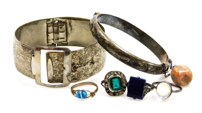 A group of costume jewellery, comprising a silver hinged bangle, three dress rings, each of Deco design set with lapis style rectangular stone, a green paste stone and an imitation moon stone, together with a plated hinged bangle. (a quantity)