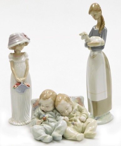 Three Lladro porcelain figures, comprising girl holding flower basket, 21cm high, girl holding lamb, 27cm high, and two sleeping babies leaning against pillar, 13cm wide.