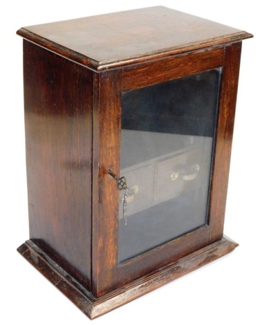 An early 20thC oak cased tobacco cabinet, with a moulded top and base, the front with a glazed door enclosing two drawers, 36cm high, 27cm wide, 20cm deep.