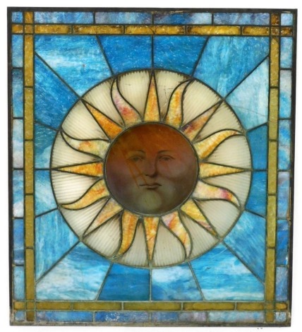 A stained glass window, decorated with the full sun, against a blue ground, 84cm high, 74cm wide.