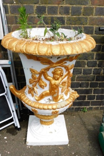 A Victorian style composition campana shaped garden urn, with a gadrooned border and decorated with putti, leaves, flowers, etc., on a tapering socle and square base, later painted white and gilt, (AF), 96cm high, 70cm wide.