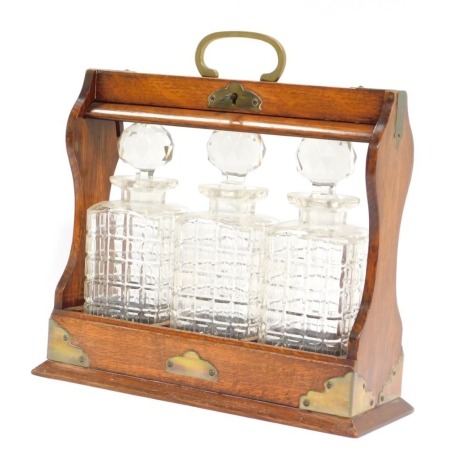 A 19thC oak tantalus, the oak case fitted with three cut glass decanters, and brass cap ends and swing handle support, with key, 35cm high, 34cm wide, 11cm deep.