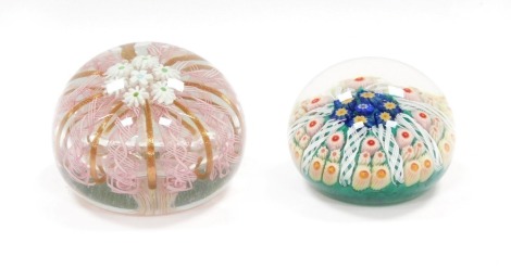 A Murano glass paperweight, decorated with daisies, pink latticino and gold ribbon strands, 9.5cm diameter, together with a concentric millefiori and latticino glass paperweight, against a green ground, 6.5cm diameter. (2)