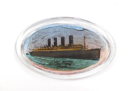 An early 20thC oval glass paperweight, decorated with the R.M.S. Mauretania, in silhouette profile, 11cm wide.