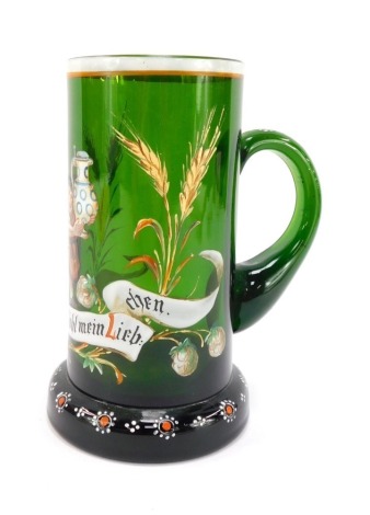 A late 19thC German green glass tankard, enamel decorated with an elfin figure holding a stein above a banner with hops and barley, reading "Dein Wohl Mein Liebchen" above a floral decorated foot, 16.5cm high.