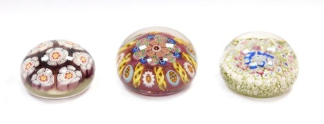 A millefiori and banded latticino glass paperweight, 8cm diameter, paperweight with seven large millefiori floral canes, 7cm diameter, and a concentric millefiori paperweight, with a pale green and silver ground, 7.5cm diameter. (3)