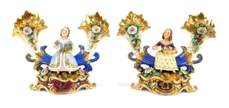 A pair of early 19thC Fischer & Mieg porcelain cornucopia vases, each encrusted with flowers and centred with a seated figure of a girl flower seller, raised on a naturalistic ground and rococo scroll base, one stamped CF324, the other F&M, 22cm wide. (AF