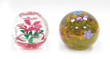 A Selkirk faceted glass paperweight, enclosing a single five petal pink flower and air bubbles, etched mark, dated 1997, 7cm diameter, and a further Selkirk butterfly paperweight, decorated with a butterfly and flowers, against a mottled moss ground, etch