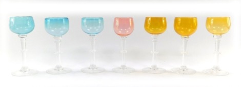 A set of seven coloured wine glasses, three blue, three green and one pink, on a clear glass stem with frilled knop, etched to foot K T Q Oylan. '75, each 19cm high. (7)